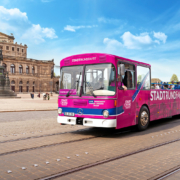 Ein pinker Stadtrundfahrt-Bus mit Gästen fährt an der Semperoper im Hintergrund vorbei, schönes Wetter